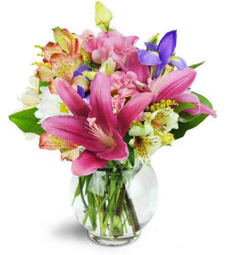 Sweet Symphony™ - Deluxe. An arrangement by Avenue Flowers and Gifts. Mauve lilies, blue iris, pink lisianthus, and more are arranged in a fluted...